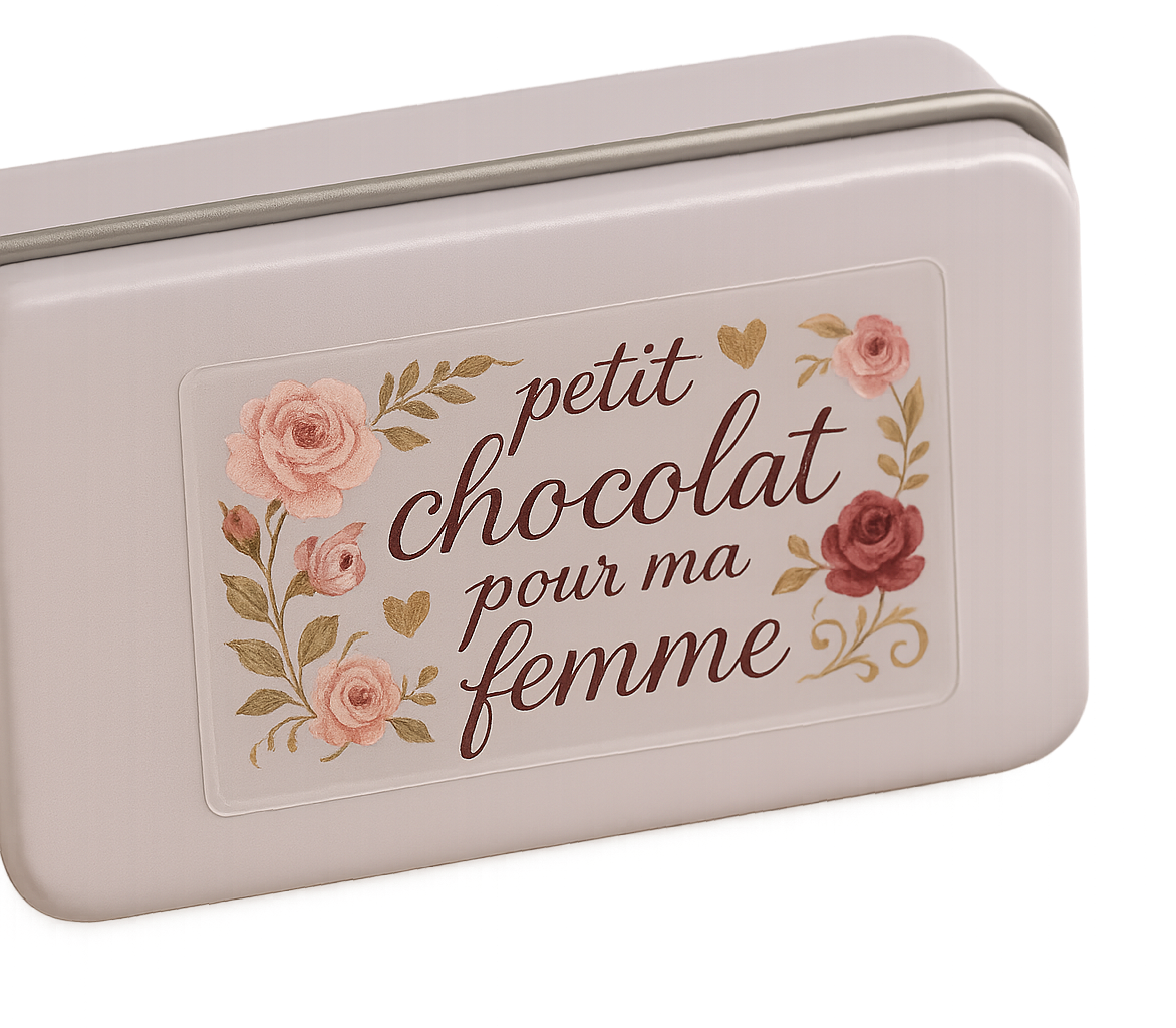a photograph of a clear rectangle sticker that is 5cm across and 2.5cm tall. The sticker is stuck onto a pale lilac biscuit tin. The sticker has a romantic multi coloured design suitable for a box of chocolates with the text ''petit chocolat pour ma femme''. The background colour of the sticker is clear.