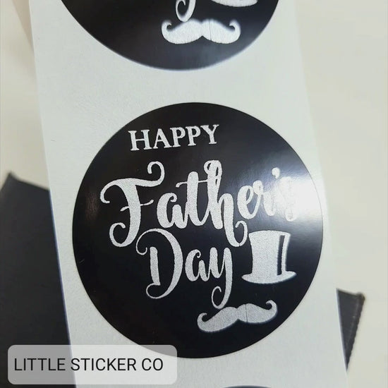Pack of Father's Day stickers. The stickers are round and glossy black with the text ''Happy Father's Day'' printed in matte silver. The stickers also have a gentleman's top hat and moustache as a printed feature.